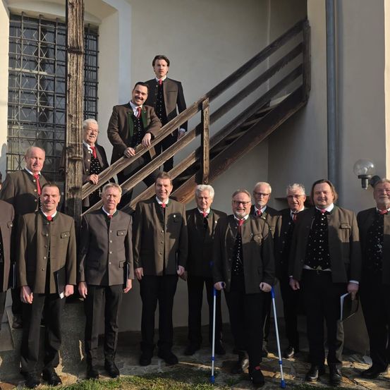 Eine Gruppe von Männern in formeller Kleidung steht vor einem Gebäude mit Treppen. Zwei Männer stehen auf den Stufen.