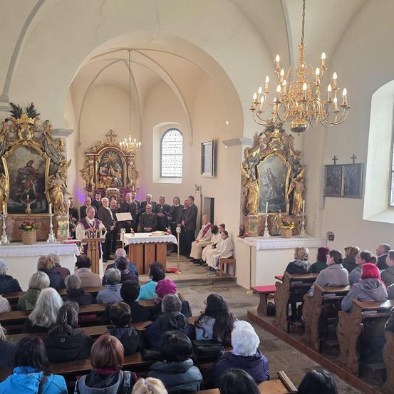 Eine Kirchenfeier mit Geistlichen und Gemeinde. Altäre, Kronleuchter und religiöse Gemälde schmücken die Wände. Der Priester steht am Altar, und die Gemeinde sitzt auf den Kirchenbänken.