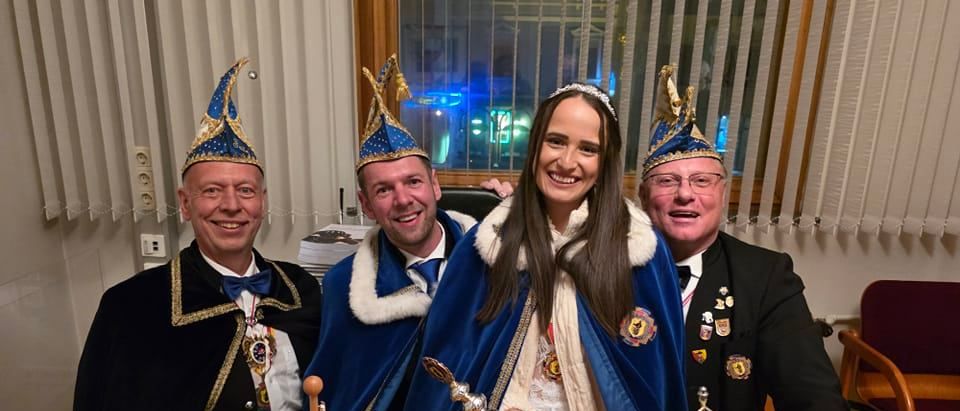 Drei Männer und eine Frau in blauer und weißer Kleidung stehen zusammen mit Flaggen und lächeln für die Kamera.