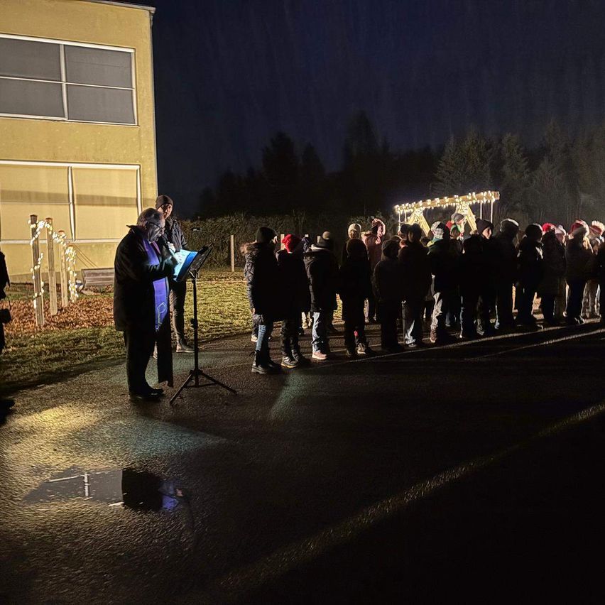 Eine Gruppe von Menschen steht nachts in einer Reihe vor einem Gebäude, mit einer Person, die auf einem Stativ mit einem Mikrofon steht.