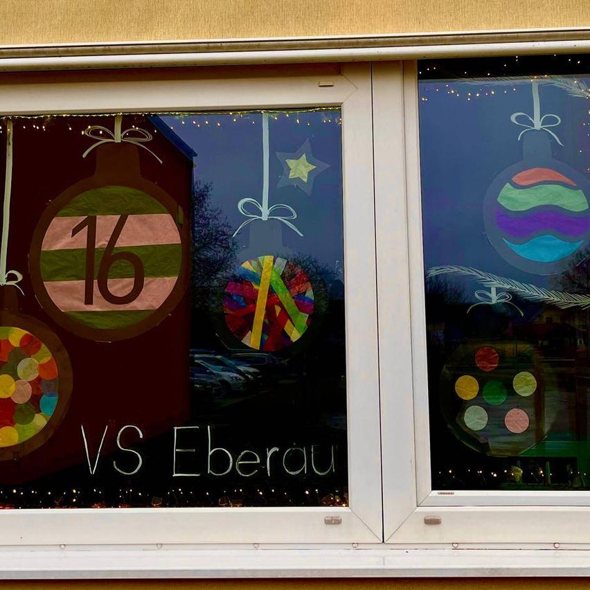 Ein Fensterdisplay zeigt einen Weihnachtsschmuck mit der Nummer 16, umgeben von anderen festlichen Ornamenten, mit den Worten 'VS Eberau' darunter geschrieben.