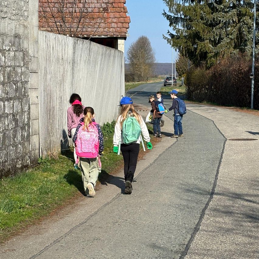 Eine Gruppe von Kindern geht auf einem Pfad. Einige tragen Handschuhe, und einige haben Rucksäcke. Ein Gebäude und Bäume sind im Hintergrund.