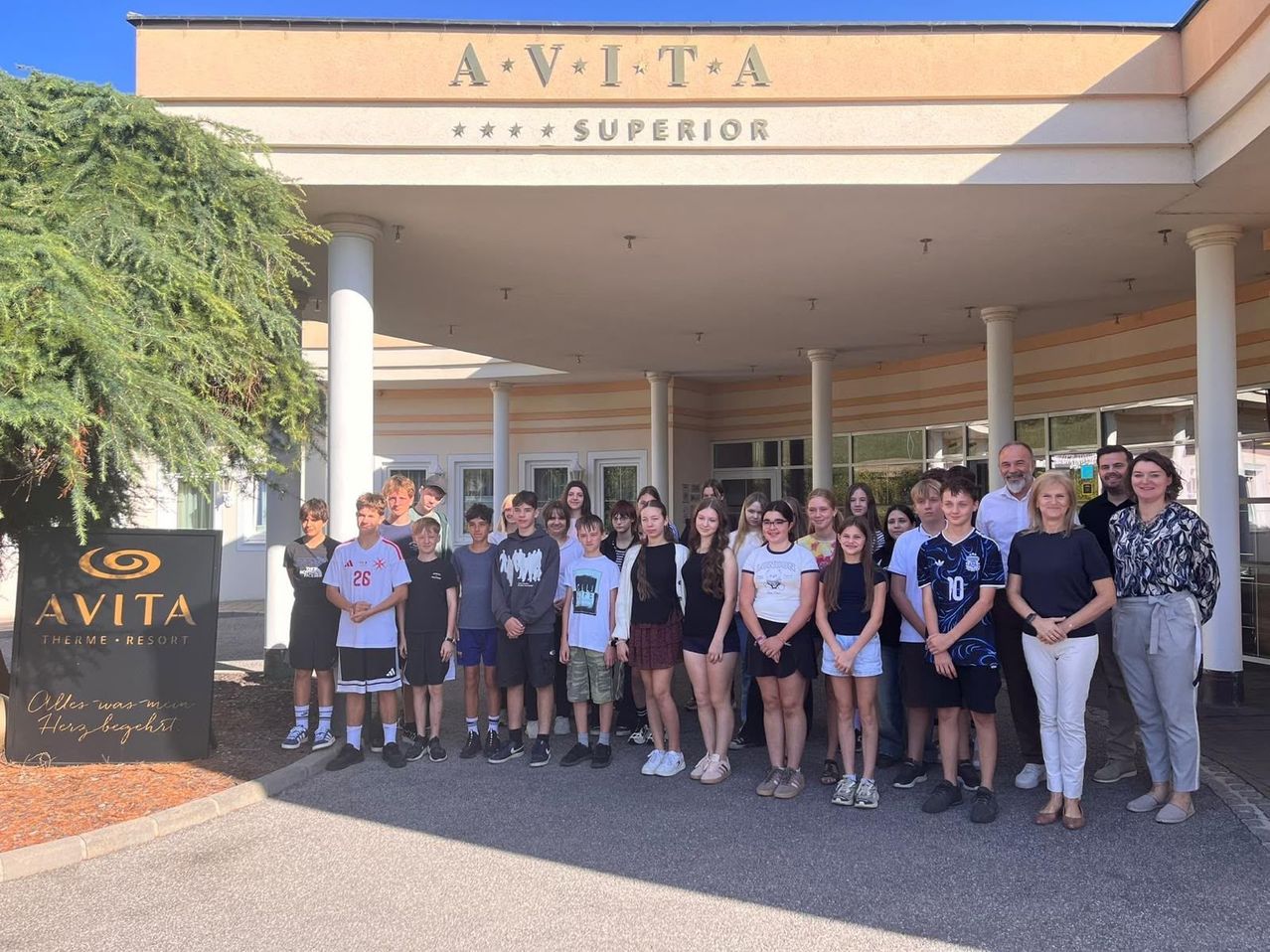 A group of students and teachers pose for a photo in front of the Avita Superior building.