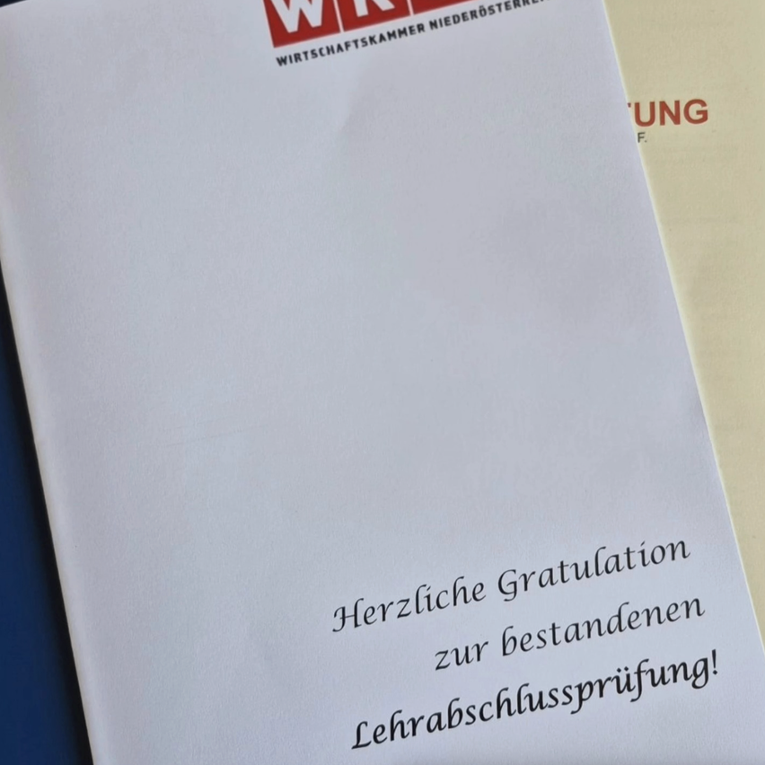Eine weiße Seite mit rotem Text darauf lautet 'Herzliche Gratulation zur bestanden!' in kursiver Handschrift. Es scheint eine Glückwunschbotschaft auf einem Zertifikat zu sein.