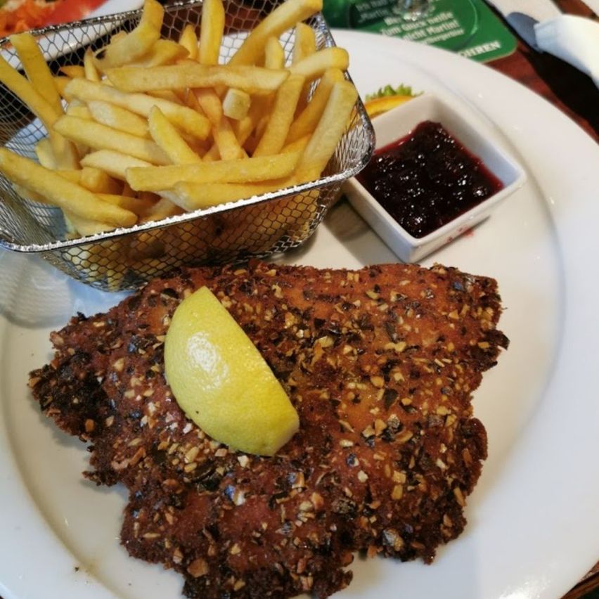 A white plate features a fried fish fillet with a lemon slice on top, accompanied by a basket of French fries and a small dish of jam.