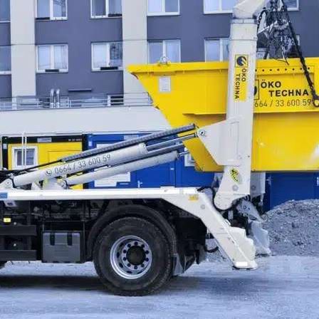 Ein weißer Lkw mit einem gelben Container davor steht vor einem Gebäude mit mehreren Fenstern.