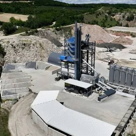 Eine Draufsicht auf eine Baustelle mit Kieshaufen und einem Maschinenfahrzeug. Links befindet sich ein Schuppen.