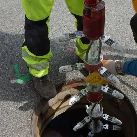 Zwei Arbeiter in neongrünen Schutzanzügen reparieren eine Maschine in einem Abwasserkanal, einer trägt einen gelben Helm und Handschuhe.