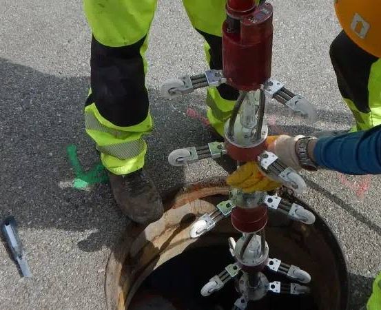 Zwei Arbeiter in neongrünen Schutzanzügen reparieren eine Maschine in einem Abwasserkanal, einer trägt einen gelben Helm und Handschuhe.
