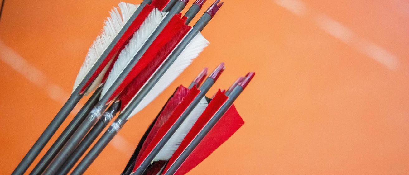 Ein Nahaufnahme von roten und weißen Pfeilen mit grauen Schäften und roten Spitzen. Die Pfeile sind ordentlich gegen einen orangefarbenen Hintergrund ausgerichtet.