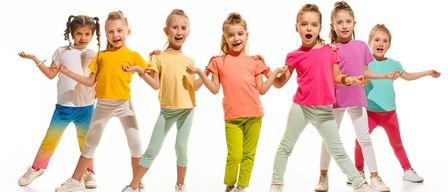 Eine Gruppe junger Mädchen in bunten T-Shirts und Leggings steht in einer Reihe, lächelt und posiert für ein Foto. Sie tragen Turnschuhe und der Hintergrund ist weiß.