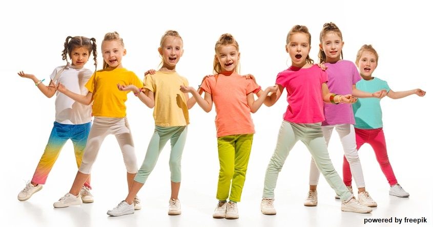 Eine Gruppe junger Mädchen in bunten T-Shirts und Leggings steht in einer Reihe, lächelt und posiert für ein Foto. Sie tragen Turnschuhe und der Hintergrund ist weiß.