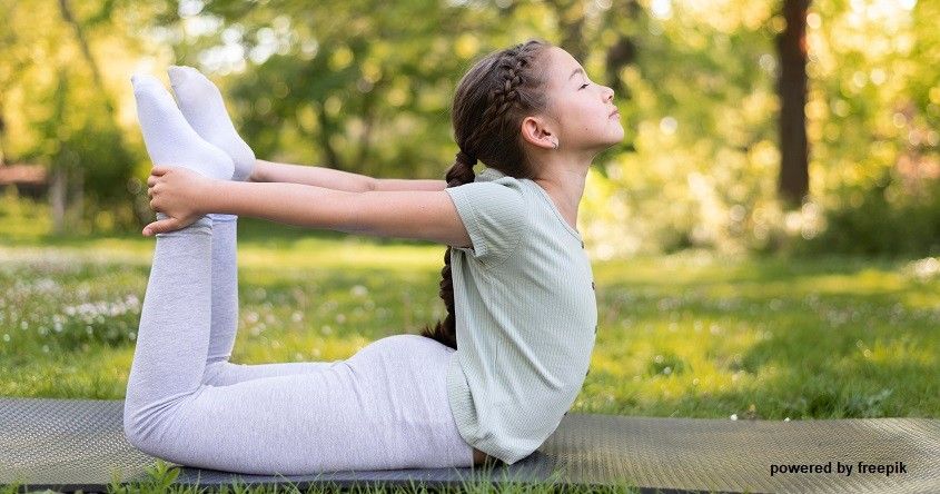 Ein junges Mädchen praktiziert Yoga auf einer Matte im Park und blickt mit geschlossenen Augen nach oben.
