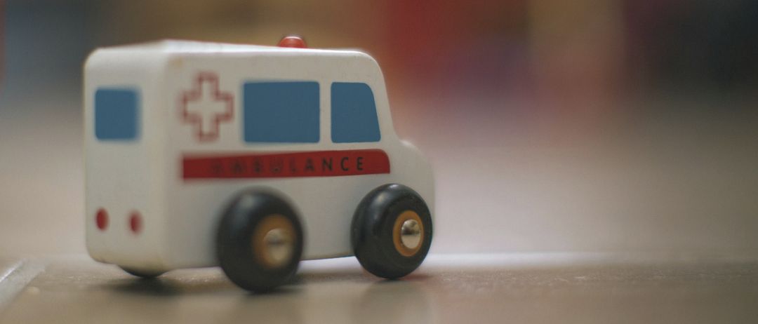 Eine Nahaufnahme eines Spielzeug-Ambulanzwagens mit einem roten Kreuz und dem Wort 'Ambulanz' in Rot auf seiner Seite geschrieben.