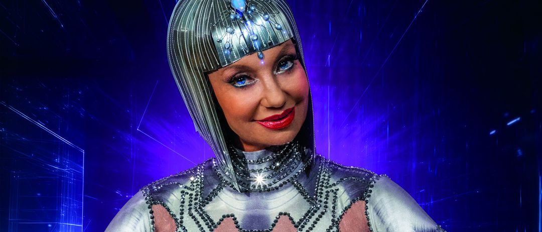 Eine Frau in einem futuristischen silbernen Kostüm mit silbernem Kopfschmuck posiert für ein Foto vor blauem Hintergrund. Der Text lautet, Eve Fast Perfekte Braut.