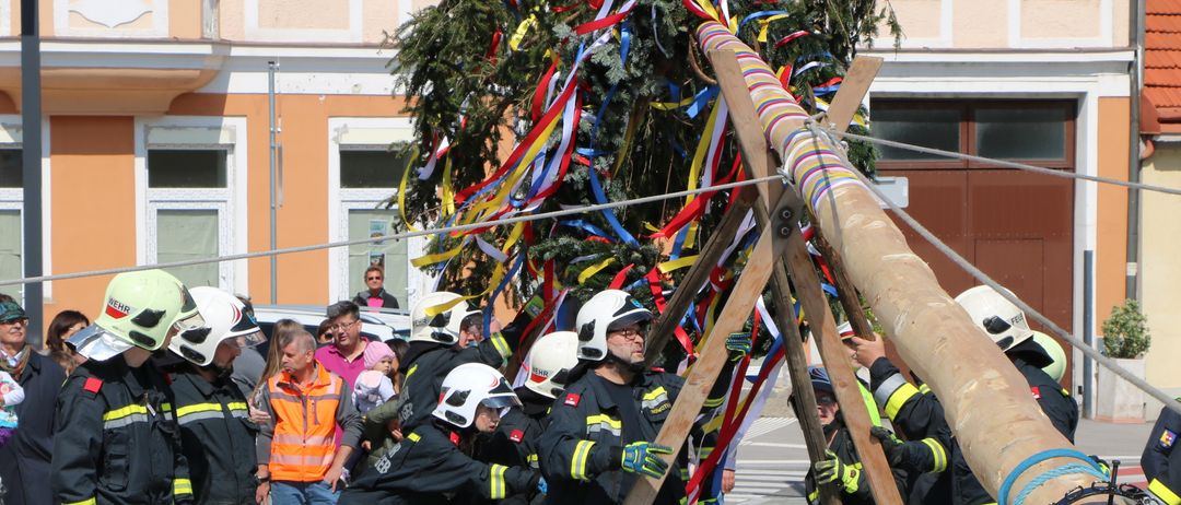 Eine Gruppe von Feuerwehrleuten in Uniform führt eine traditionelle Baumfällzeremonie in einem städtischen Bereich durch.