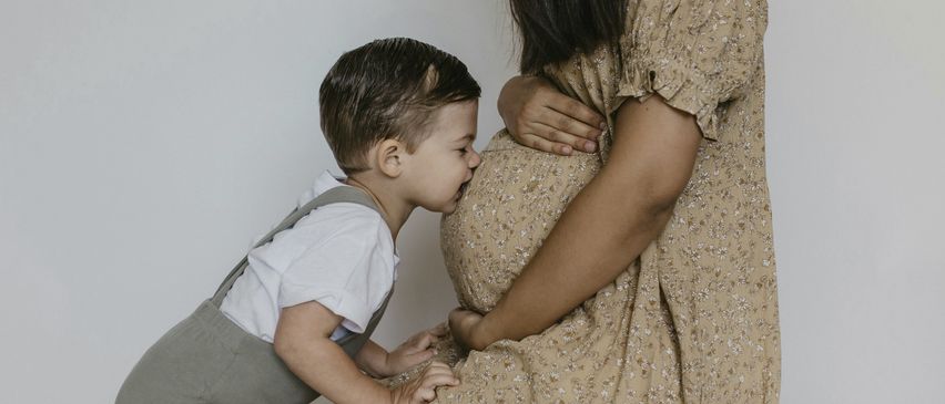 Ein kleiner Junge küsst den Bauch seiner schwangeren Mutter in einer Studioumgebung.