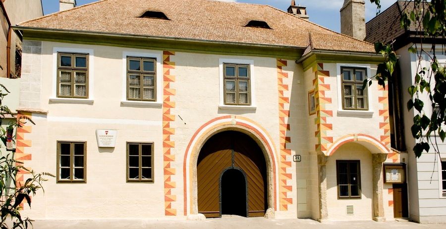 Ein dreistöckiges weißes Gebäude mit einem braunen Dach. Es hat mehrere Fenster mit Gittern und eine Holztür.