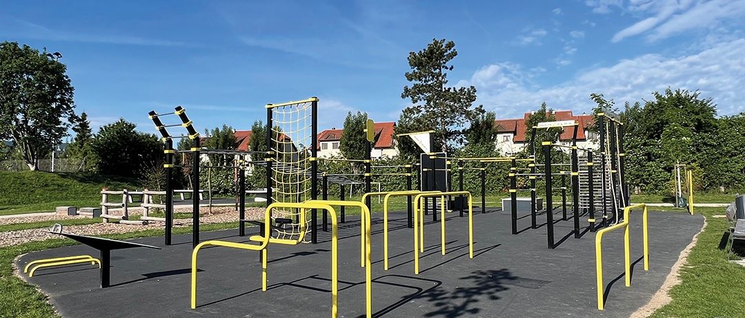 Ein Outdoor-Fitnesspark mit gelben Trainingsstangen und Kletterstrukturen unter blauem Himmel.
