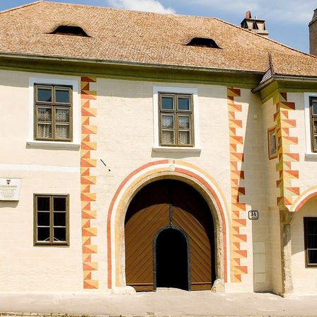 Ein altes Haus mit einem Ziegeldach und einem gewölbten Holztor. Das Haus hat mehrere Fenster und dekorative geometrische Muster an den Wänden. Über der Tür befindet sich die Nummer 34 an der Wand.