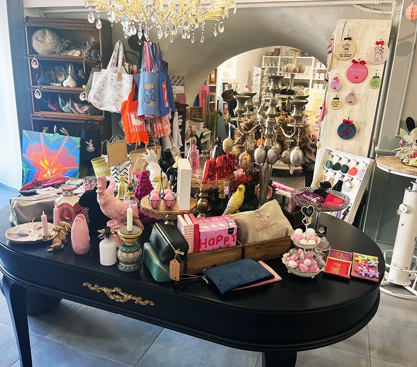 Ein Raum mit verschiedenen ausgestellten Gegenständen, darunter Handtaschen, Ornamente und Dekorationsartikel auf einem Tisch, mit einer Kronleuchter darüber.