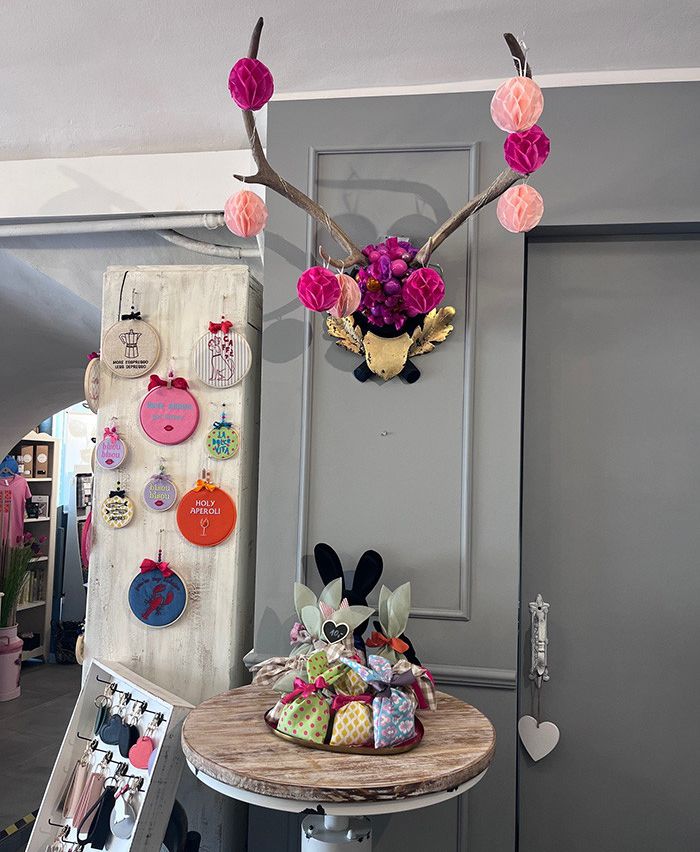 Ein Tisch mit einem Blumen-Rehkopf und einem Korb mit Geschenktüten, vor einem grauen Hintergrund, und eine Wand mit verschiedenen Dekorationen.