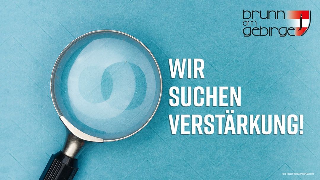 Eine Lupe mit den Worten 'WIR SUCHEN VERSTÄRKU' auf blauem Hintergrund. Die Lupe reflektiert Licht und wirkt verschwommen.