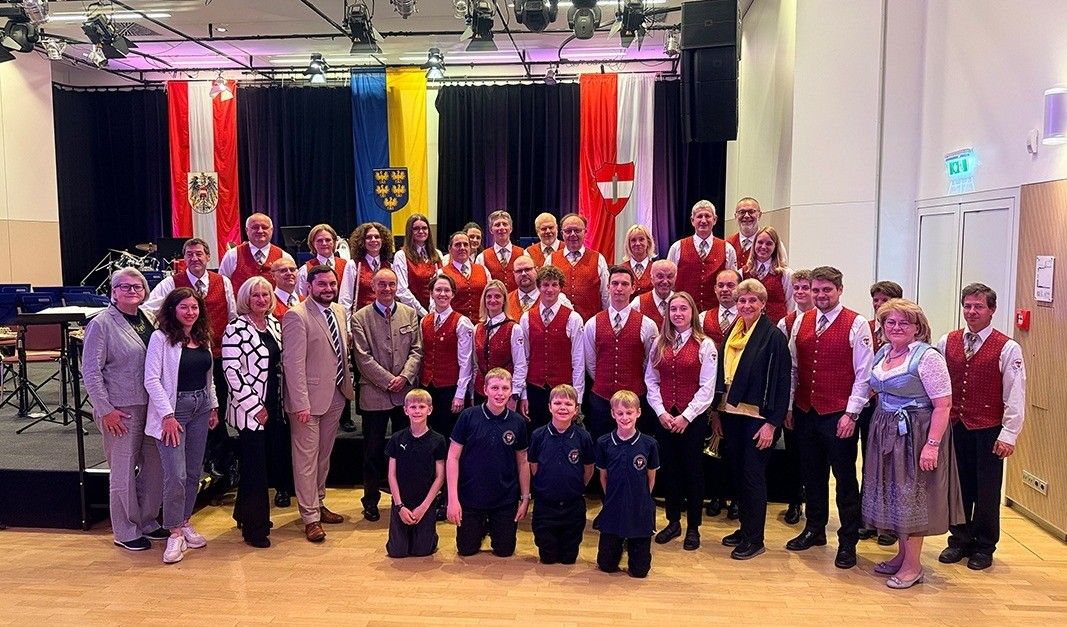 Gruppe von Erwachsenen und Kindern in traditioneller Kleidung posiert für ein Foto mit Fahnen im Hintergrund.