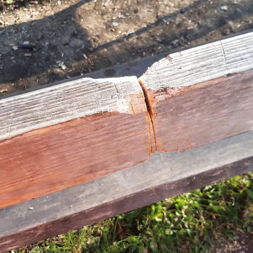 A close-up view of a wooden plank with a visible crack and dirt and debris on the ground.