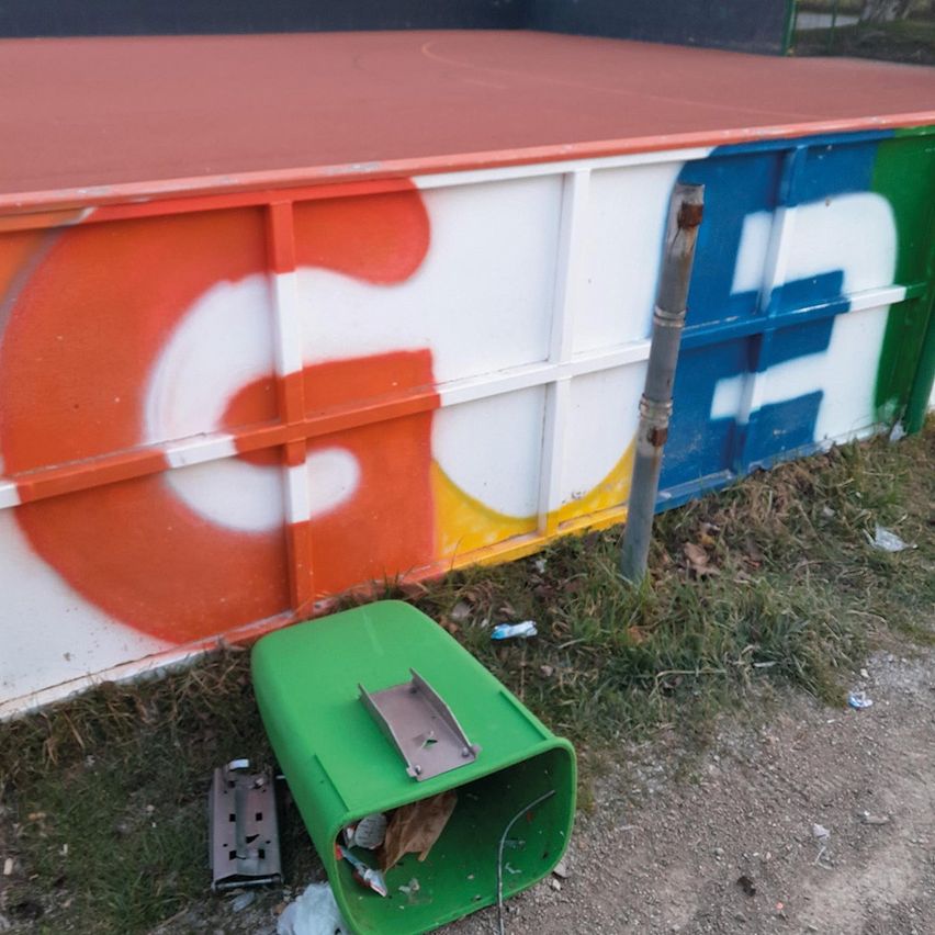 A graffiti-covered wall with the letter 'C' in orange, white, and yellow. Below it, a green trash bin is open on the ground.