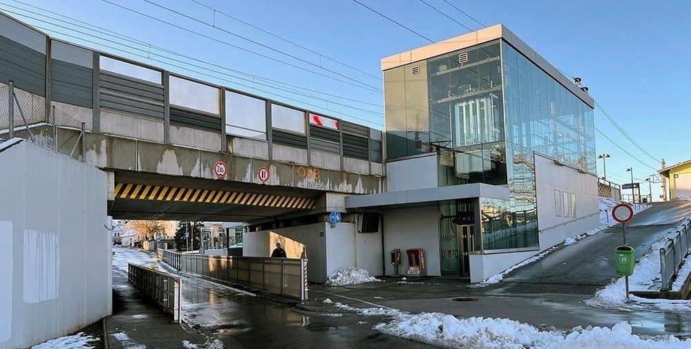 Eine Fußgängerbrücke über einer Straße mit einem Gebäude rechts, einer Person, die geht, und einem schneebedeckten Bürgersteig.