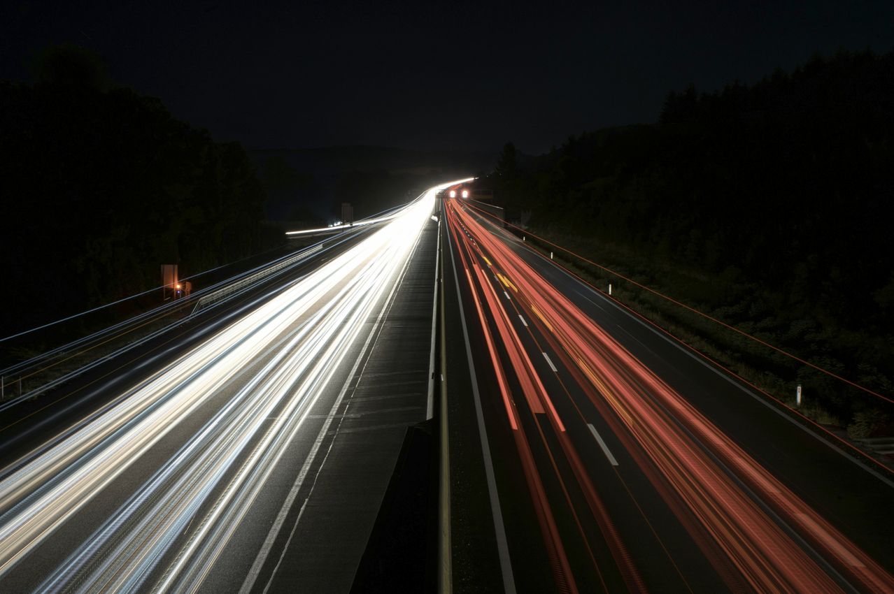 Eine nächtliche Autobahn mit mehreren Spuren, beleuchtet von Autoscheinwerfern, die gestreifte Lichter von fahrenden Fahrzeugen zeigen.