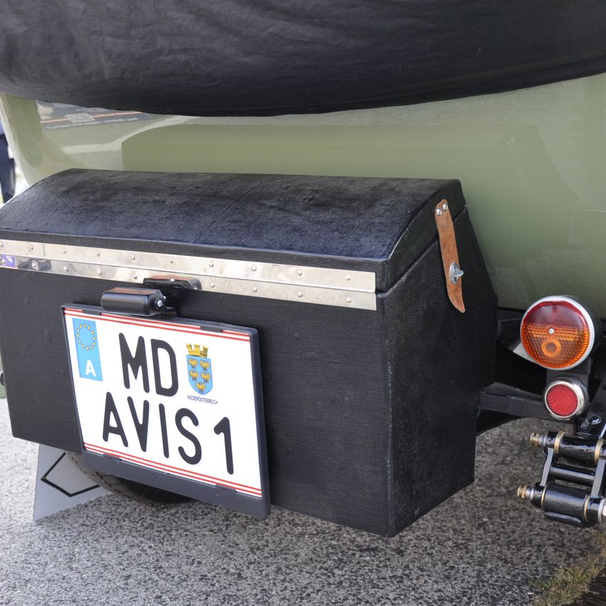 Die Rückseite eines Oldtimers mit einer schwarzen Aufbewahrungsbox, einem Nummernschild mit der Aufschrift 'MD AVI51' und einem roten Rücklicht.