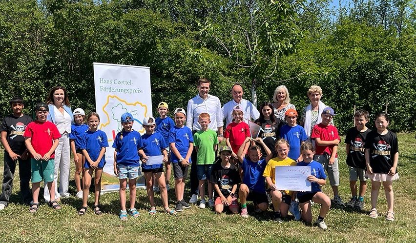 Eine Gruppe von Kindern und Erwachsenen posiert für ein Foto auf einem Grasfeld mit einem Banner dahinter.
