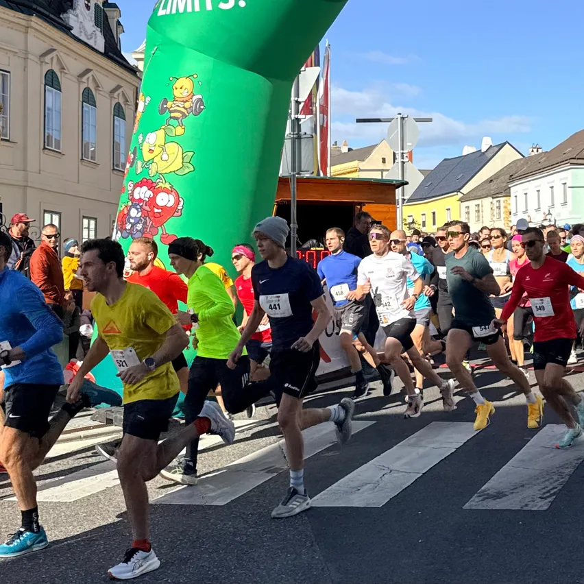 Läufer starten einen Lauf unter grünem Torbogen in einer österreichischen Stadt.