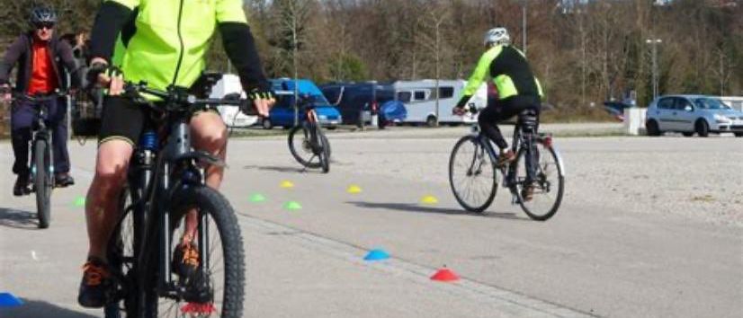 Eine Gruppe von Radfahrern fährt auf einer Straße, mit Kegel und anderen Fahrzeugen im Hintergrund.