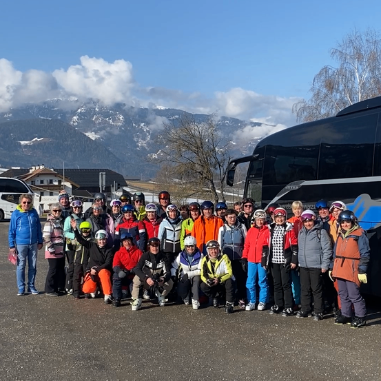 Eine Gruppe von Menschen in Winterkleidung steht vor einem Bus, mit verschneiten Bergen im Hintergrund.