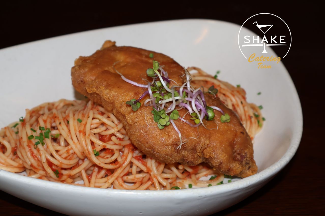 Ein Teller mit gebratenem Fisch auf Spaghetti mit roter Sauce und grünen Kräutern. Das Gericht ist mit roten Zwiebeln garniert.