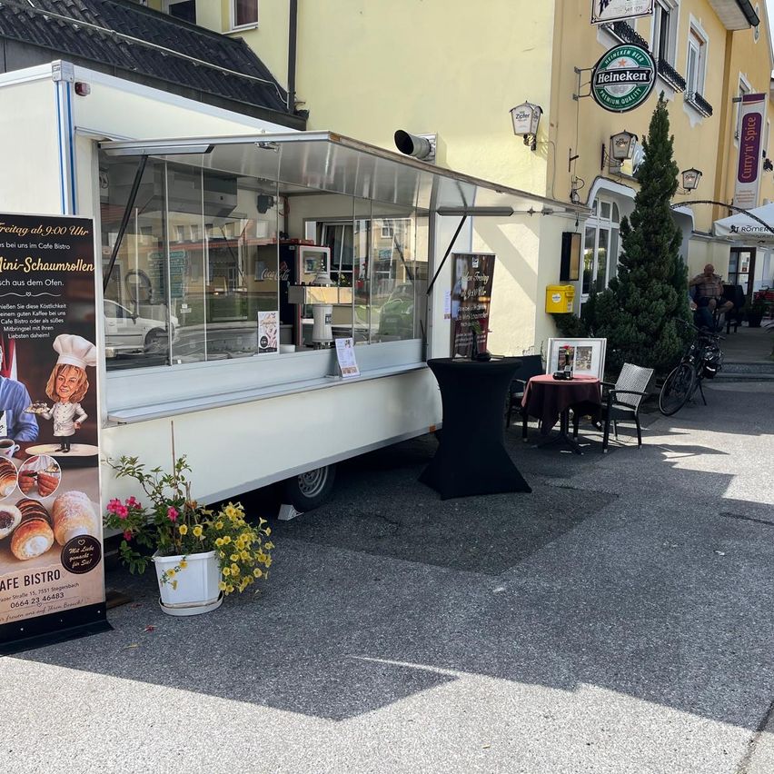 Ein Essenswagen, der an der Straße geparkt ist, mit einem Banner, das für ein Café-Bistro wirbt. Ein Topf mit Pflanzen und ein Fahrrad sind in der Nähe.