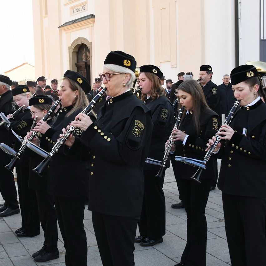 A group of women in uniform stand in line, holding clarinets, performing in front of a church.
