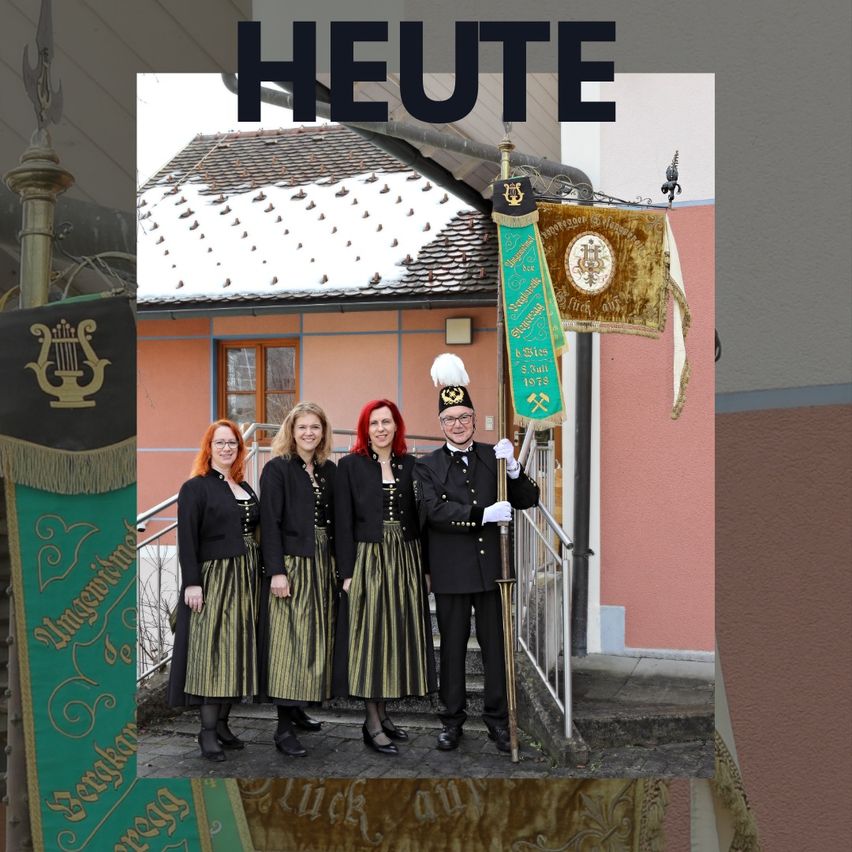 A group of people dressed in traditional attire stand on steps in front of a building. Three women and a man are posing. Behind them, banners and flags are displayed.
