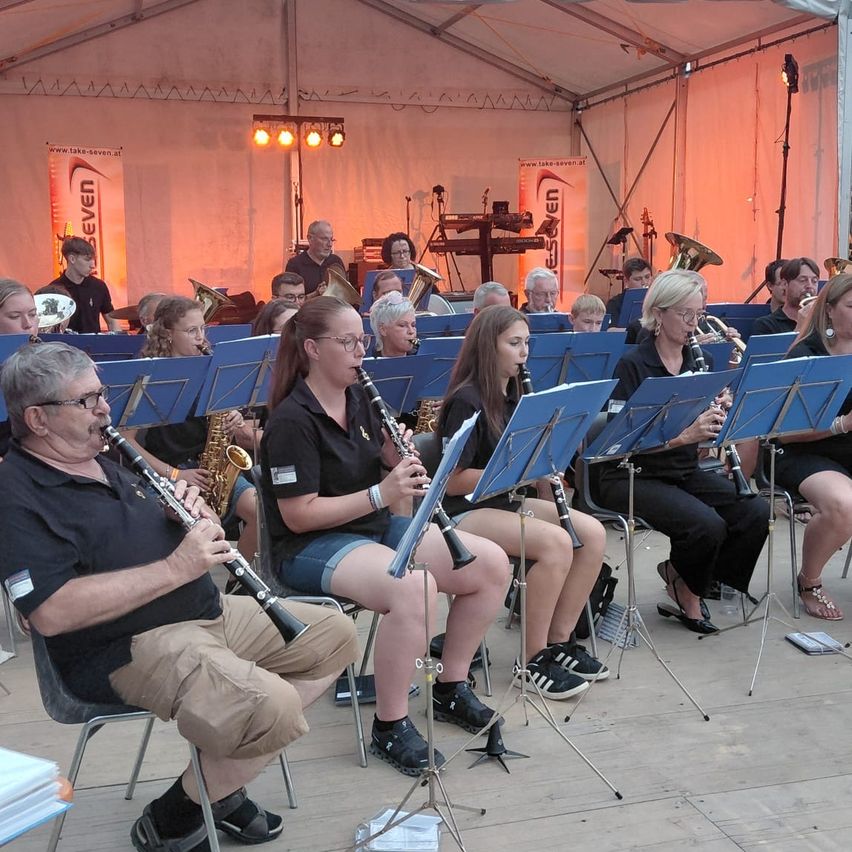 Eine Gruppe von Musikern, darunter Klarinettisten, Saxophonisten und Trompeter, spielt auf der Bühne in einem Zelt. Die Musiker sitzen und stehen, einige halten ihre Instrumente.