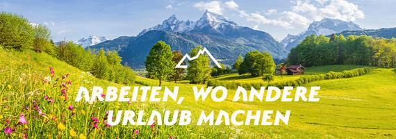 Eine malerische Ansicht eines üppigen grünen Tals mit Bergen im Hintergrund. Im Vordergrund befindet sich eine farbenfrohe Wiese mit verschiedenen Blumen und einem kleinen Haus. Das Bild enthält ein Logo und eine Textüberlagerung, die 'Arbeiten, wo andere Urlaub machen' lautet.