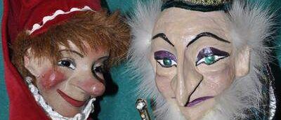 Two puppets are standing close to each other. The puppet on the left is wearing a red hat and a red outfit. The puppet on the right is wearing a black hat and a white fur around the neck.