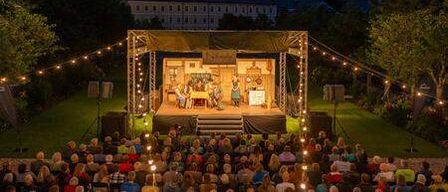 A nighttime performance in an outdoor setting with a stage, audience, and scenic backdrop.