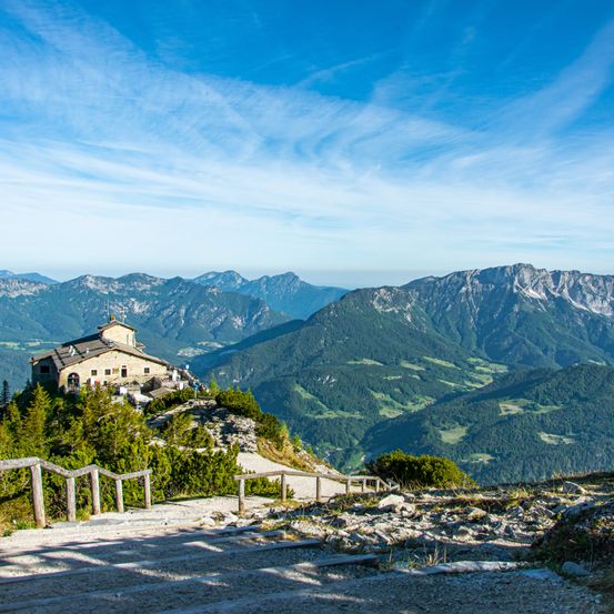 Ein Chalet auf einem Berggipfel mit klarem blauem Himmel und majestätischen Bergen im Hintergrund.