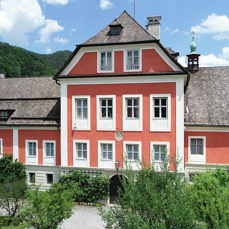 Ein großes rotes und weißes Gebäude mit vielen Fenstern und einer grünen Dachkuppel steht vor dem Hintergrund von Bergen und blauem Himmel.