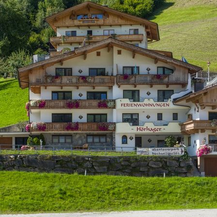 Ein großes Chalet mit Holzbalkonen und Blumenkästen steht vor einem grünen Hang. Der Name Horhager ist deutlich auf der Vorderseite angebracht.