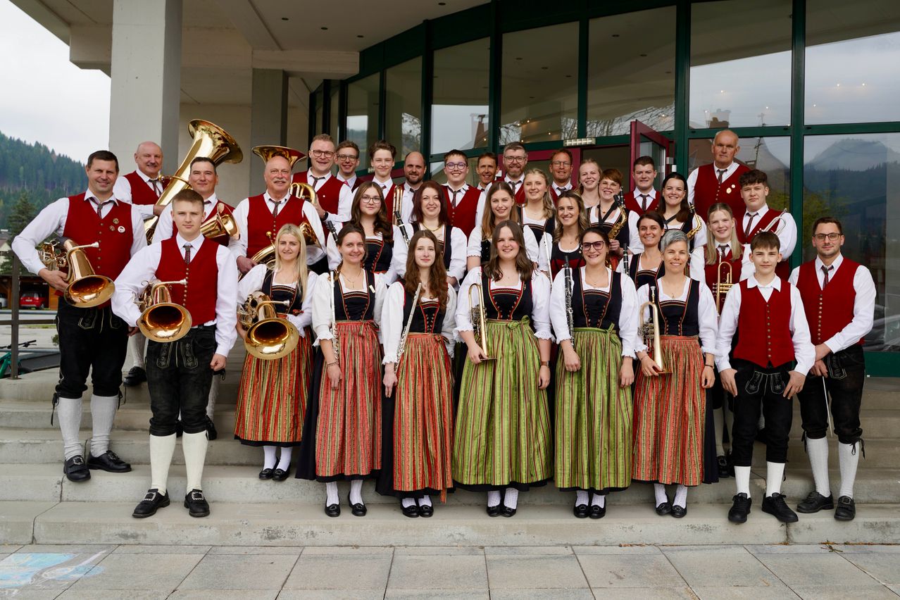 Eine Gruppe von Musikern in traditioneller Kleidung, die auf einer Treppe stehen und Blechblasinstrumente halten, posiert für ein Foto.