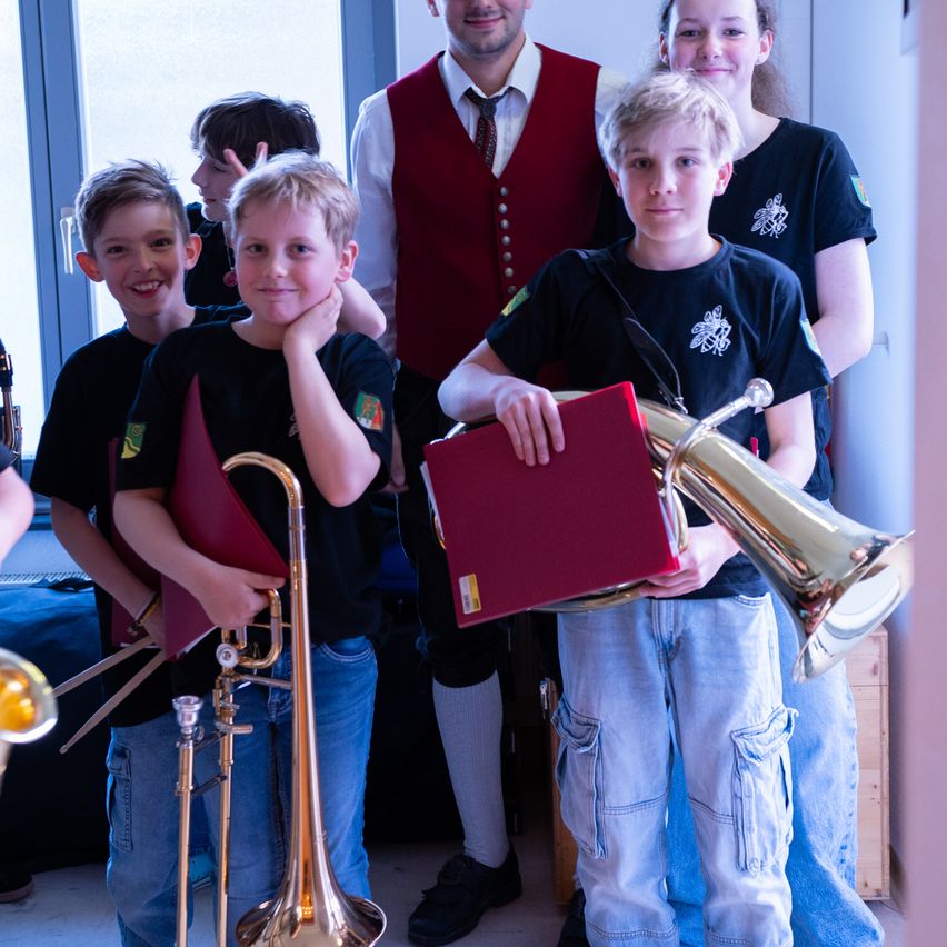 Fünf junge Jungen und zwei Erwachsene posieren für ein Foto. Sie halten Musikinstrumente, darunter ein Posaune, Tuba und Trompete.